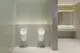 Weiße Wand mit zwei Urinalen, links und rechts montiert, umgeben von grauer und mintgrüner Wandverkleidung. Ideal Standard Waschbecken im Hintergrund mit zwei Wasserhähnen.